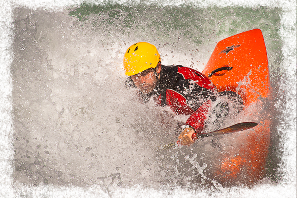 Person wearing a yellow helmet and red jacket kayaking through rough whitewater, surrounded by splashing water.