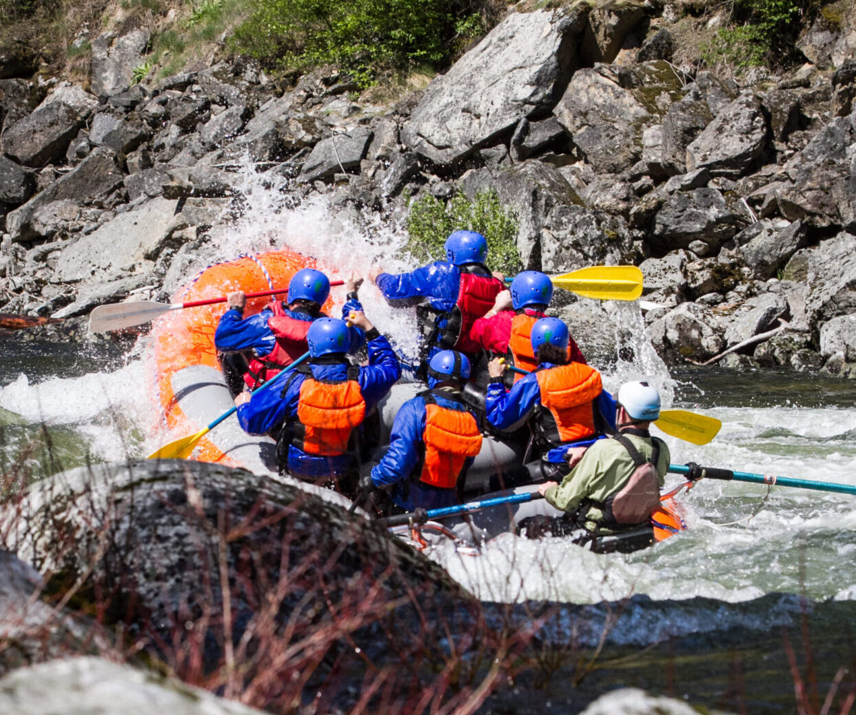 A group of people wearing helmets and life jackets paddle a raft through whitewater rapids surrounded by rocks, enjoying one of the thrilling Lochsa River attractions.