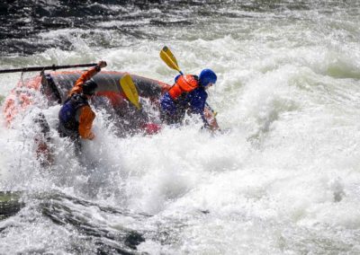 Two rafters in helmets and life jackets navigate a massive whitewater rapid on the Lochsa River, surrounded by churning whitewater.