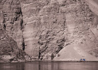 A small raft with a group of rafters floats along the Alberton Gorge, dwarfed by towering purple-hued canyon walls.