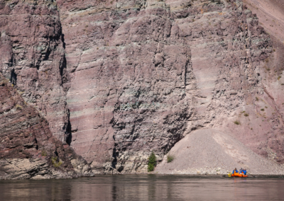 A small raft with a group of rafters floats along the Alberton Gorge, dwarfed by towering purple-hued canyon walls.