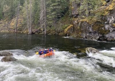 A group of rafters paddling through a scenic rapid on the Lochsa River, surrounded by forest on a guided trip