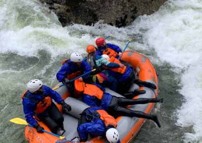 Rafters getting back into the raft after falling out during a whitewater adventure on the Lochsa River with Zoo Town Surfers. The group, in vibrant safety gear, shows resilience and teamwork as they recover in the midst of the challenging rapids. White water fun!